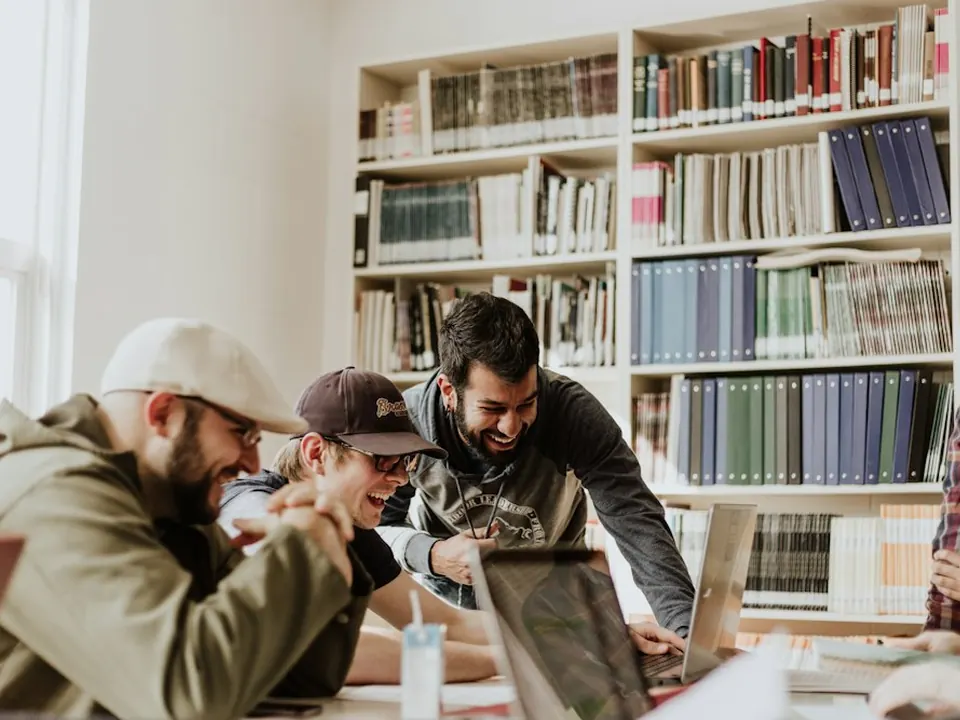 Grupo de estudantes sorrindo enquanto estudam juntos em notebooks na biblioteca